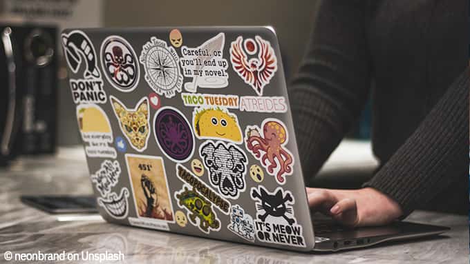 Un ordinateur portable ouvert, posé sur une table. Le dos de l'écran est couvert de stickers colorés.