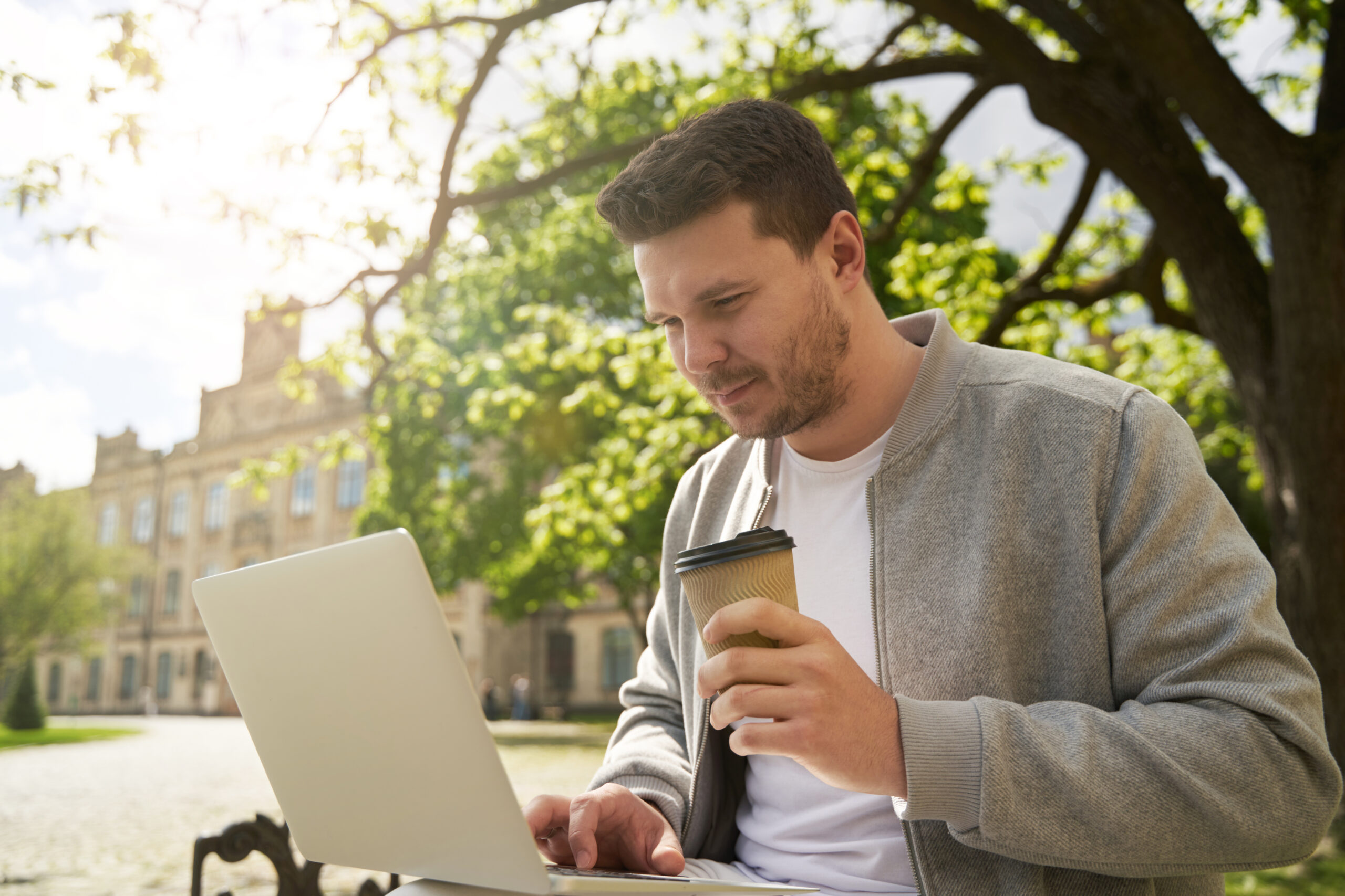 Homme freelance travaillant sur son ordinateur portable tout en buvant un café dans un espace extérieur verdoyant, symbolisant la flexibilité et l'indépendance du travail à distance.